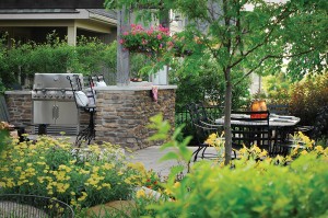 Hanging planters and landscaped gardens add to the appeal of this outdoor kitchen and dining room designed by The Landmark Group.