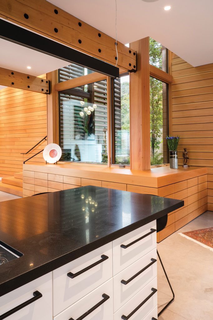 The kitchen island (right) opens onto the vertical window indent, which brings in natural light during the day and scatters artistic reflections throughout the room as the sun sets.