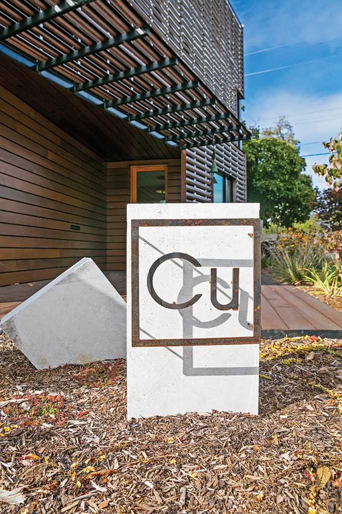 the stone and copper sculpture with Cu, the periodical table symbol for copper (right) perched where the driveway meets the carved-out triangular entry porch.