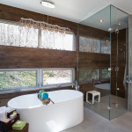 A standing soaker tub adds a sculptural element to the master bathroom. Two window walls open to a view of the woods. Porcelain tile adorns both walls and floor.