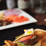 A Black Angus chipotle bison burger with lettuce, tomato, pickles, onion, cheese and a fried quail egg, with deep fried pickles on the side.