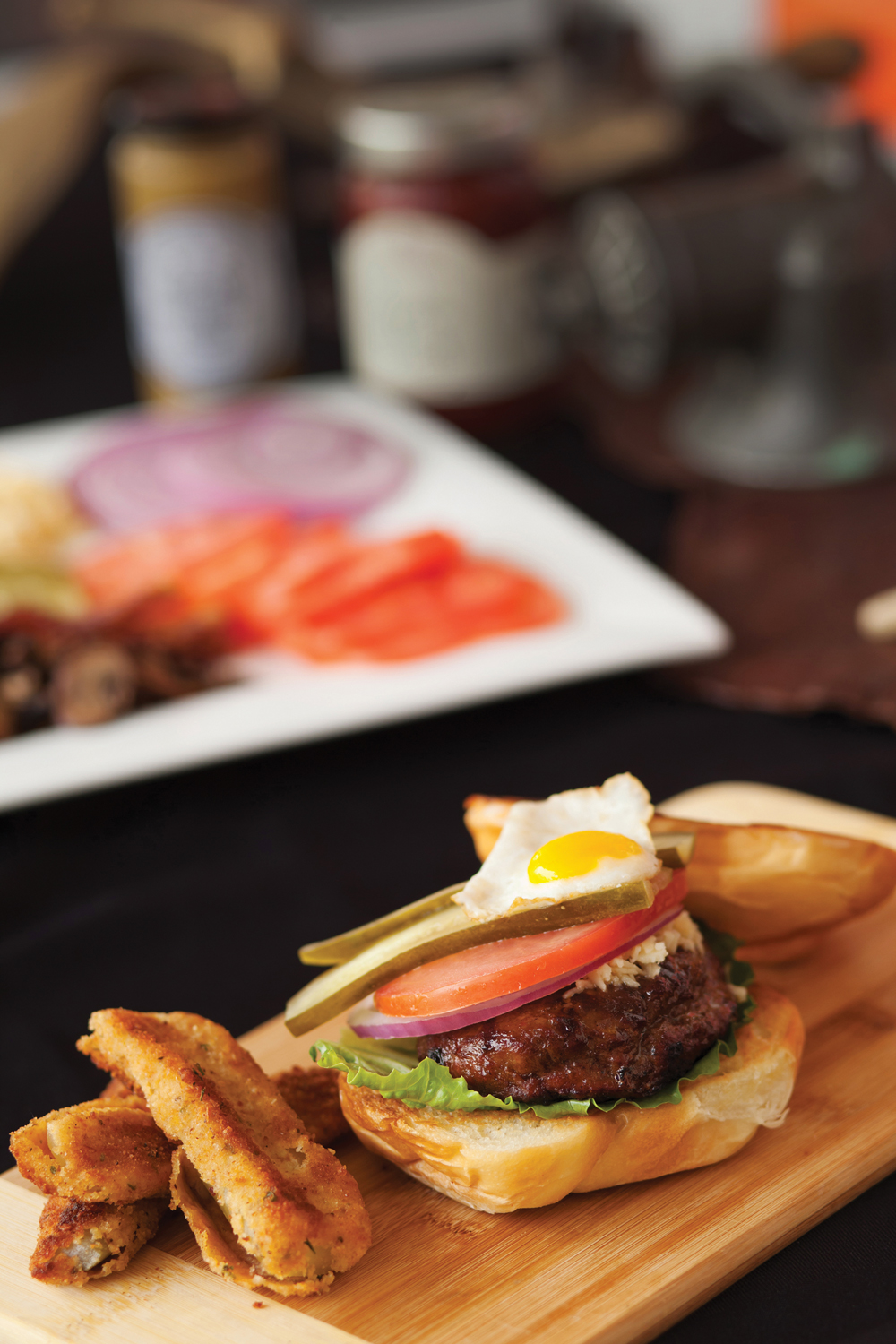 A Black Angus chipotle bison burger with lettuce, tomato, pickles, onion, cheese and a fried quail egg, with deep fried pickles on the side.