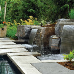 Sheets of water tumble from stacked boulders into the swimming pool while stone slabs create an attractive walkway.