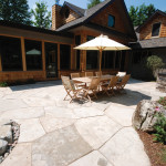 The new sunroom opens onto an outdoor eating area and flagstone patio overlooking rail fences and farm fields. A stone path meanders by a hot tub before passing under a wooden trellis on its way to the pool area.