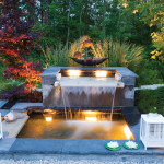 Water pours over a limestone slab into a small pond in a garden designed by Gordon J. Leece Landscapes. At night, creative lighting adds a dramatic element.
