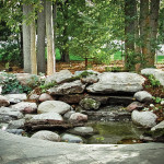 A wooded lot provides the perfect backdrop for a water feature in this garden designed by Natural Stonescapes.