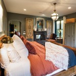 Dark grey walls and clay-red bedding and upholstery work well together in the mainfloor master bedroom. On the other side of the see-through fireplace is a small den.