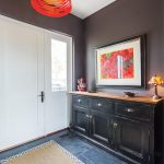 Doors in the breezeway open to a mudroom. Slate flooring is a practical choice in the mudroom entrance. The drum light pendant by Foscanini is from Lumens. Art by Lila Lewis Irving. Sisal carpet from Mackenzie-Childs.