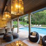 A stone staircase leads from the house to the resort-like pool area. The covered living space boasts a fireplace, TV, dining table and kitchen. The oversize pendant lights are from Sescolite.
