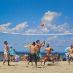 Beach volleyball players enjoy a game at Wasaga Beach while other beachgoers of all ages partake in a variety of activities on sand and water.