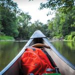 A small backpack with supplies – sunscreen, insect repellent, water, snacks and rain gear – sits in the bow of the canoe, within easy reach (