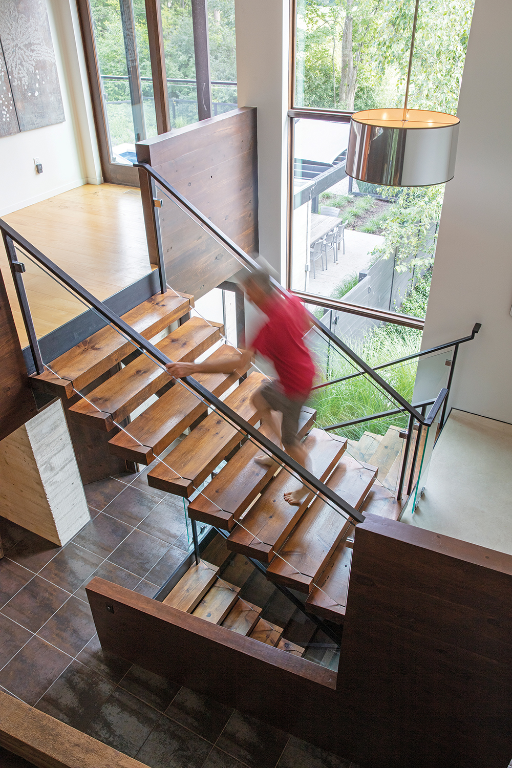 The open staircase is an architectural marvel of floating pine steps, glass sides and black metal railings lit by a multi-level vertical window during the day and a contemporary chrome chandelier at night. “The stairs are not rectangular,” notes Campbell. “They’re at a slight angle, which is not only more interesting but also more functional to give you a path of least resistance from point A to point B.” The upper level has loft workspaces that are open to the level below.